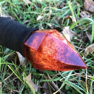May include: A wooden staff with a black leather wrap and a red and orange resin crystal tip.