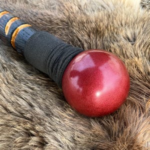 May include: A wooden walking stick with a black leather wrap and a red, round, metallic ball on the end.