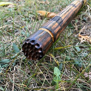 Op de afbeelding: Close-up van een houten wandelstok met een getextureerd, honingraat-achtig ontwerp aan het uiteinde. De stok is donkerbruin met een lichtere bruine band in het midden.