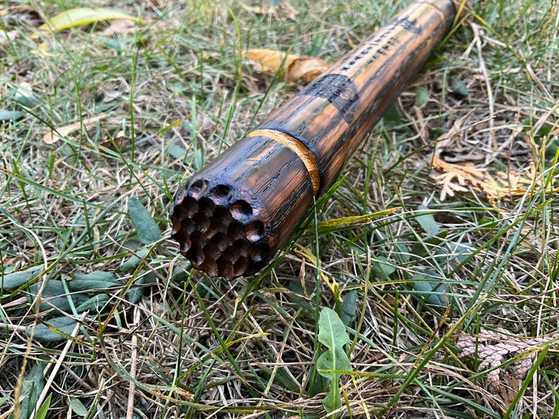 Op de afbeelding: Close-up van een houten wandelstok met een getextureerd, honingraat-achtig ontwerp aan het uiteinde. De stok is donkerbruin met een lichtere bruine band in het midden.