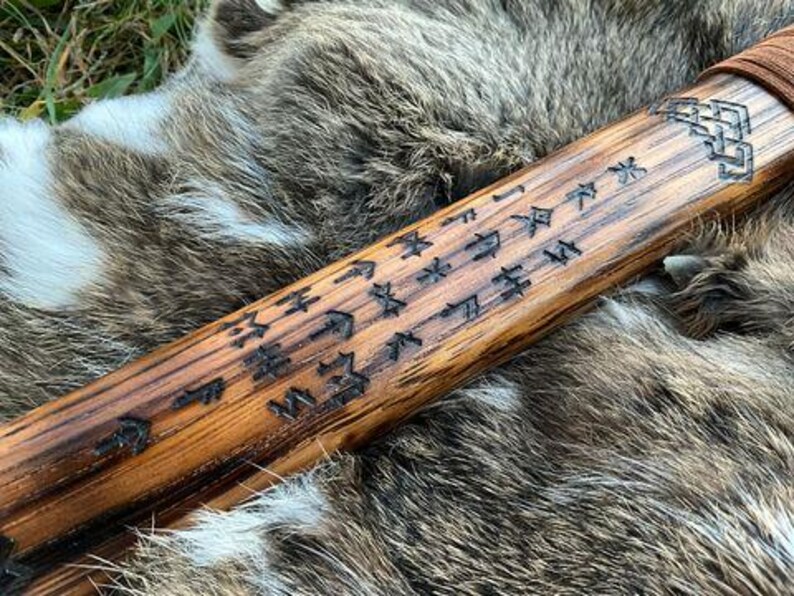 May include: A wooden staff with intricate carvings and runes. The staff is brown and has a natural wood finish. The runes are carved into the wood and are visible against the light brown background.