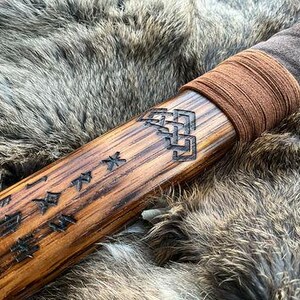 May include: A wooden staff with a brown leather wrap and intricate carvings. The staff is decorated with Japanese characters and a knotwork design.
