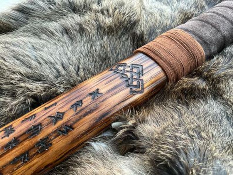 May include: A wooden staff with a brown leather wrap and intricate carvings. The staff is decorated with Japanese characters and a knotwork design.