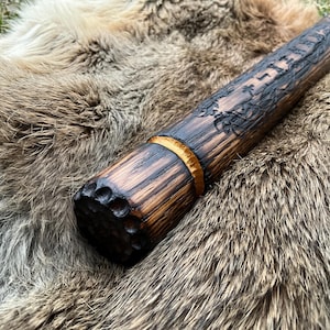 May include: A wooden club with a dark brown finish and a gold band around the top. The club is decorated with intricate carvings and has a textured surface.