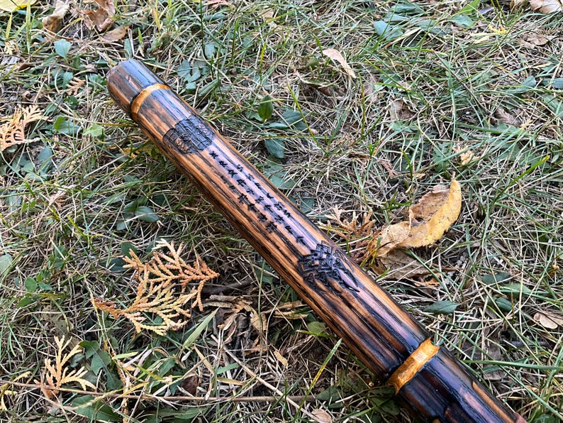 Op de afbeelding: Een houten wandelstok met een donkerbruine vlek en gouden accenten. De stok heeft een gesneden ontwerp en een inscriptie.
