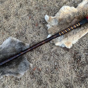 May include: A wooden staff with a red and black ball on the end. The staff is wrapped in gold tape and has a black tip.