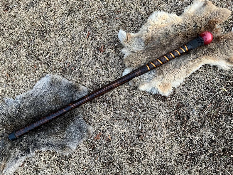 May include: A wooden staff with a red and black ball on the end. The staff is wrapped in gold tape and has a black tip.