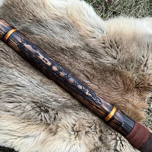 May include: A wooden staff with a dark brown finish and gold accents. The staff is decorated with intricate carvings and a brown leather wrap at the bottom.