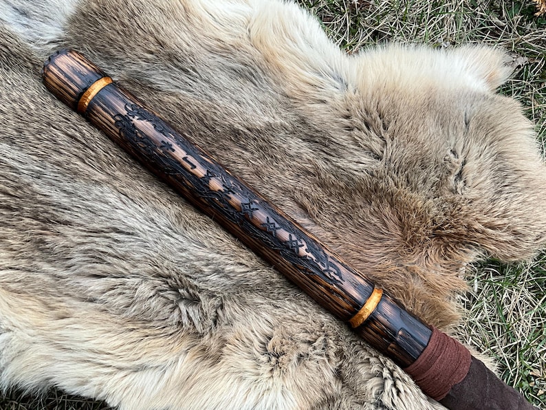 May include: A wooden staff with a dark brown finish and gold accents. The staff is decorated with intricate carvings and a brown leather wrap at the bottom.