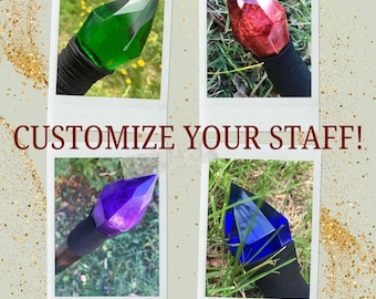 May include: Four different colored crystal topped staffs. The crystals are green, red, purple, and blue. The staffs are made of wood and have a black wrap around the bottom. The text "CUSTOMIZE YOUR STAFF!" is displayed in the center of the image. The text "TheUnassailableMage.com" is displayed at the bottom of the image.
