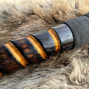 May include: A wooden staff with a black and gold spiral design. The staff is wrapped in black leather at the top.