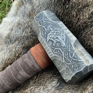 May include: A silver metal hammer with a brown leather handle. The hammer head has a detailed design of a wolf and a Celtic knot.