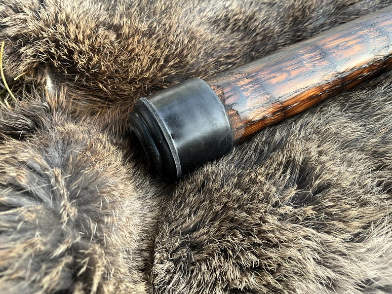 May include: A wooden walking stick with a black rubber tip. The stick has a dark brown finish and a natural wood grain.