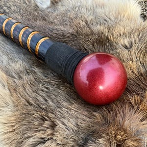 May include: A wooden walking stick with a black and gold patterned handle and a red ball on the end.