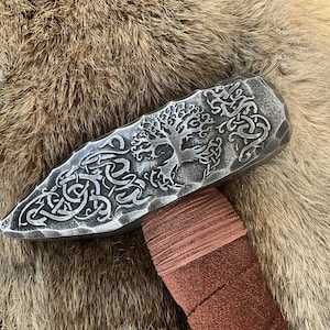 May include: A silver metal hammer head with a detailed design of a tree and intricate patterns. The hammer head is wrapped in brown leather.