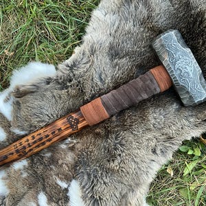 May include: A wooden-handled hammer with a leather wrap and a steel head. The head is engraved with a wolf design and runes. The handle is also engraved with runes.