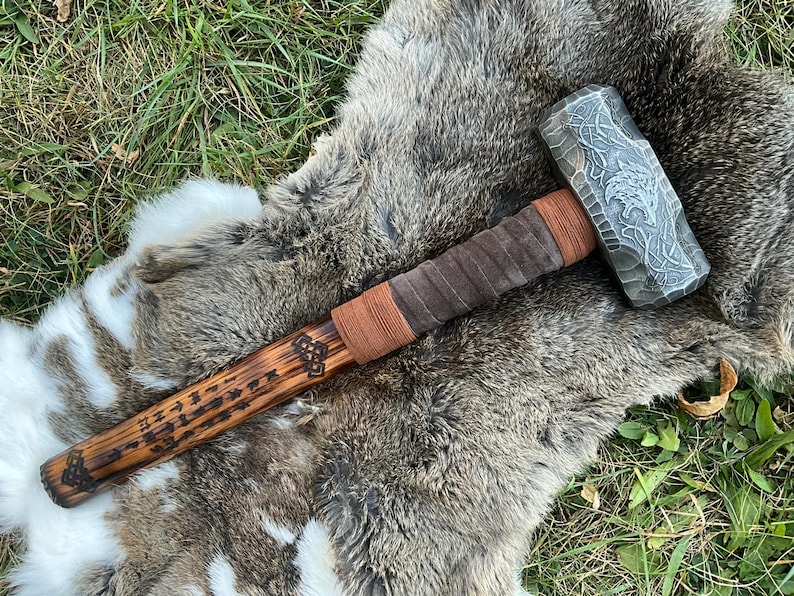 May include: A wooden-handled hammer with a leather wrap and a steel head. The head is engraved with a wolf design and runes. The handle is also engraved with runes.