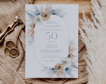 May include: An invitation card for a 50th birthday celebration, featuring floral arrangements in blue, beige, and white. The card includes the text "Shhh... ES UNA SORPRESA!" and the name "LUCIA FERNANDEZ". A gold wax seal and stamp are visible.