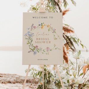 May include: A welcome sign for a bridal shower with a floral wreath design. The sign is on a wooden easel and says "Welcome to Emilia's Bridal Shower 24.04.202X".