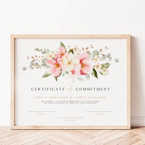 May include: A certificate of commitment with a floral design featuring pink and white flowers and green leaves. The text reads "CERTIFICATE of COMMITMENT" and "EMILIA WILLIAMS & JAMES WILLIAMS DECLARED A LIFETIME COMMITMENT TO EACH OTHER ON THIS 24TH DAY OF APRIL IN THE YEAR 202X".