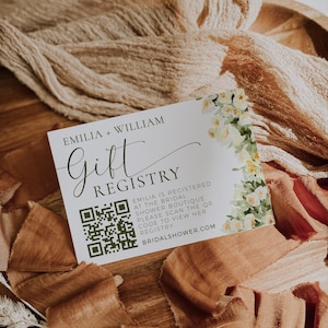 May include: A white gift registry card with the names "EMILIA + WILLIAM" and the word "Gift Registry" in elegant script. The card features a QR code and floral accents. The website address is BRIDALSHOWER.COM.