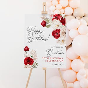 Könnte beinhalten: Ein weißes Schild auf einer Holzstaffelei mit der Aufschrift "Happy Birthday!" und "welcome to Emilia's 50th Birthday Celebration 24 April 202x". Das Schild ist mit roten und weißen Blumen verziert und von Luftballons umgeben.