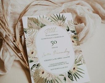 May include: A white invitation card with floral and botanical illustrations. The card features text in Spanish, including "50 años de Lucia Fernandez" and event details. The design incorporates beige, green, and gold tones, with a soft, neutral background.