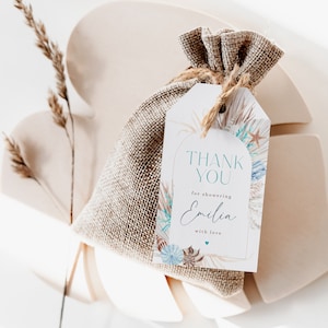 May include: A white thank you tag with a gold border and a watercolour design of seashells and palm leaves. The tag says "Thank You for showering Emilia with love". The tag is tied to a small hessian bag.