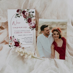 May include: A wedding invitation with a floral design in shades of burgundy, pink, and green. The invitation features a gold arch and the text "Nos casamos" in a cursive font. The text below the arch reads "Te invitamos cordialmente a boda de CARLOS + LUCIA SABADO ABRIL 24 13:00PM Calle cualquier 123 cualquier lugar, ep: 12345 Recepci&oacute;n a Seguir Por favor, confirmar su asistencia a Maria 123-456-78-90".