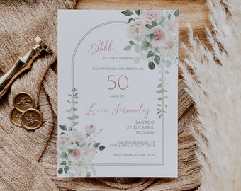May include: A white invitation card with floral accents and text. The card features a floral design with pink and white flowers and green leaves. The text reads "Shhh... Es una sorpresa" and details for a 50th birthday celebration.