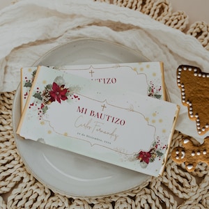 May include: Two rectangular chocolate bars with white wrappers featuring a gold frame, red poinsettia flowers, and green holly leaves. The text reads MI BAUTIZO, Carlos Fernandez, and 24 de Diciembre, 202x, with a small cross symbol above.