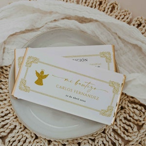 May include: Two white chocolate bars with gold foil wrapping, featuring gold text and a gold angel illustration. The bars are on a white plate, with text that reads "mi bautizo" and the name "Carlos Fernandez".