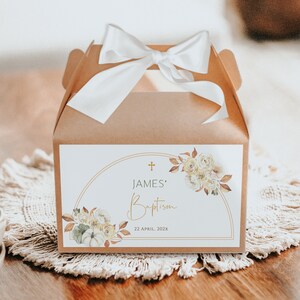 Può includere: Una scatola regalo marrone con un nastro di raso bianco e un fiocco. La scatola ha un'etichetta bianca con una croce dorata, il testo "JAMES' Baptism" e la data "22 APRIL, 202X". L'etichetta è decorata con un'illustrazione ad acquerello di rose bianche, zucche e foglie autunnali.
