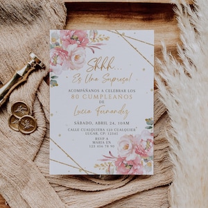 Op de afbeelding: Een uitnodigingskaart met roze bloemen en gouden details, die een 80e verjaardag aankondigt. De tekst is in het Spaans. Het bloemendesign wordt aangevuld met gouden geometrische lijnen op een neutrale achtergrond.