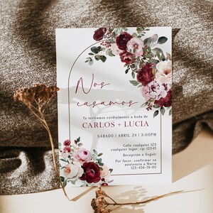 May include: A wedding invitation with a floral design in shades of pink and burgundy. The invitation reads "Nos casamos" which translates to "We are getting married". The invitation also includes the names Carlos and Lucia, the date and time of the wedding, and the address of the ceremony.