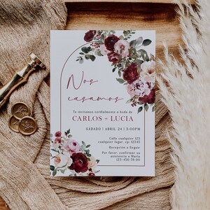 May include: A wedding invitation with a watercolor floral design in shades of burgundy, pink, and white. The text reads "Nos casamos" which translates to "We are getting married" in English. The invitation includes the names Carlos and Lucia, the date Saturday, April 24, and the time 3:00 PM. It also includes a phone number for RSVP.