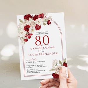 Puede incluir: Una tarjeta de invitación blanca con un diseño floral con rosas rojas y blancas. La tarjeta anuncia una celebración del 80 cumpleaños de Lucía Fernández, con la fecha y hora del evento. El texto es de color burdeos.