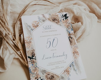 May include: A white invitation card with a floral design featuring beige and blue flowers. The text on the card reads "Skkk... ES UNA SORPRESA! ACOMPAÑANOS A CELEBRAR LOS 50 AÑOS DE Lucia Fernandez CALLE CUALQUIERA 123 CUALQUIER LUGAR. CP: 12345 RSVP MARIA 123 456 7890"