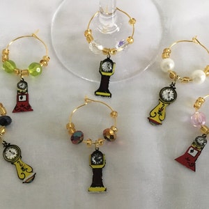 May include: Five gold-colored wine glass charms with different colored beads and a clock charm. The charms are hanging from gold hoops.