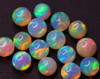 May include: A collection of fourteen round, polished opal gemstones. Each stone features a translucent, milky white base with vibrant, iridescent flashes of green, orange, and blue colour play visible across the smooth, spherical surfaces.