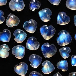 Puede incluir: Una colecci&oacute;n de peque&ntilde;os cabujones de piedra lunar en forma de coraz&oacute;n que presentan un aspecto transl&uacute;cido con una distintiva adularescencia azul. Cada piedra individual muestra una superficie lisa y pulida con una silueta de coraz&oacute;n redondeada.