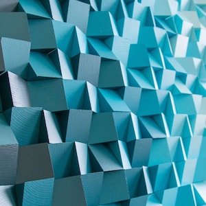 Pode incluir: Uma peça de arte de parede feita de cubos de madeira, pintados em tons de azul, branco e cinza. Os cubos são dispostos em um padrão geométrico, criando um efeito 3D.