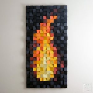 Puede incluir: Una pieza de arte mural rectangular de madera con un diseño de llama. La obra de arte está compuesta por pequeños bloques de madera cuadrados en tonos negros, naranjas, amarillos y rojos, creando un efecto texturizado y tridimensional. El diseño de la llama está centrado sobre un fondo oscuro.
