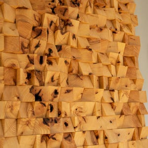 Könnte beinhalten: Eine Wand aus kleinen, unregelmäßig geformten Holzblöcken. Die Blöcke sind in einem Muster angeordnet, das eine strukturierte Oberfläche erzeugt. Das Holz ist hellbraun mit dunkelbraunen Knoten und Maserung.