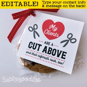 May include: A white card with red and black text and graphics. The card says "My Clients Are A Cut Above and their referrals rock, too!" with a red heart and scissors graphics. The card is attached to a clear bag with a chocolate chip cookie inside.