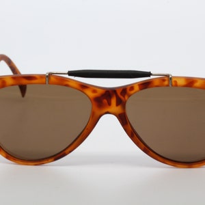 Op de afbeelding: Schildpadzonnebril met bruine glazen en een zwarte band over de brug.