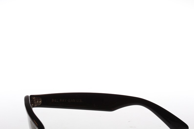 Peut inclure: Gros plan sur la branche en plastique noire d'une paire de lunettes de soleil. La branche est grav&eacute;e du texte "B&L RAY-BAN U.S."