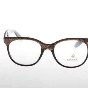 Könnte beinhalten: Braune und schwarze gemusterte Brille mit klaren Gläsern. Der Markenname "BARRAGE" ist auf dem rechten Glas aufgedruckt.