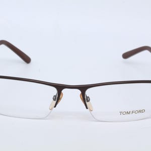 May include: Brown metal frame eyeglasses with clear lenses. The brand name "TOM FORD" is printed on the right lens.