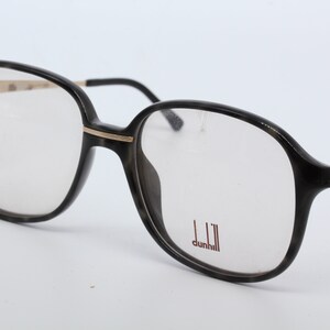 May include: Black tortoise shell eyeglasses with gold accents and the brand name "dunhill" printed on the right lens.